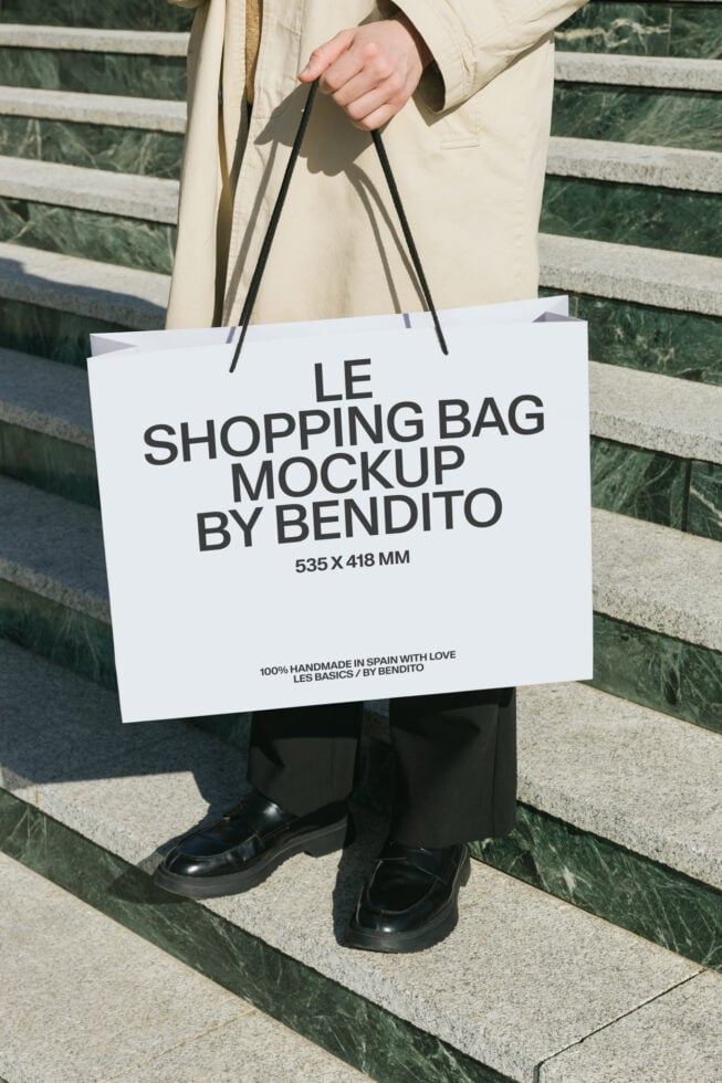 Person holding white shopping bag mockup in beige coat outdoors