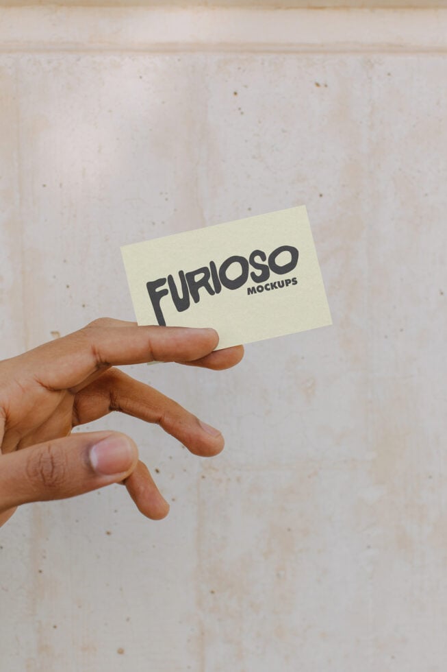 Hand presenting pale yellow business card featuring dark Furioso Mockups branding