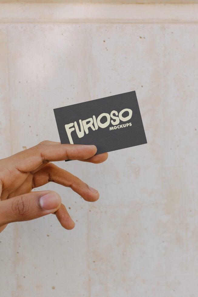 Fingers displaying dark business card with cream Furioso Mockups text on speckled backdrop