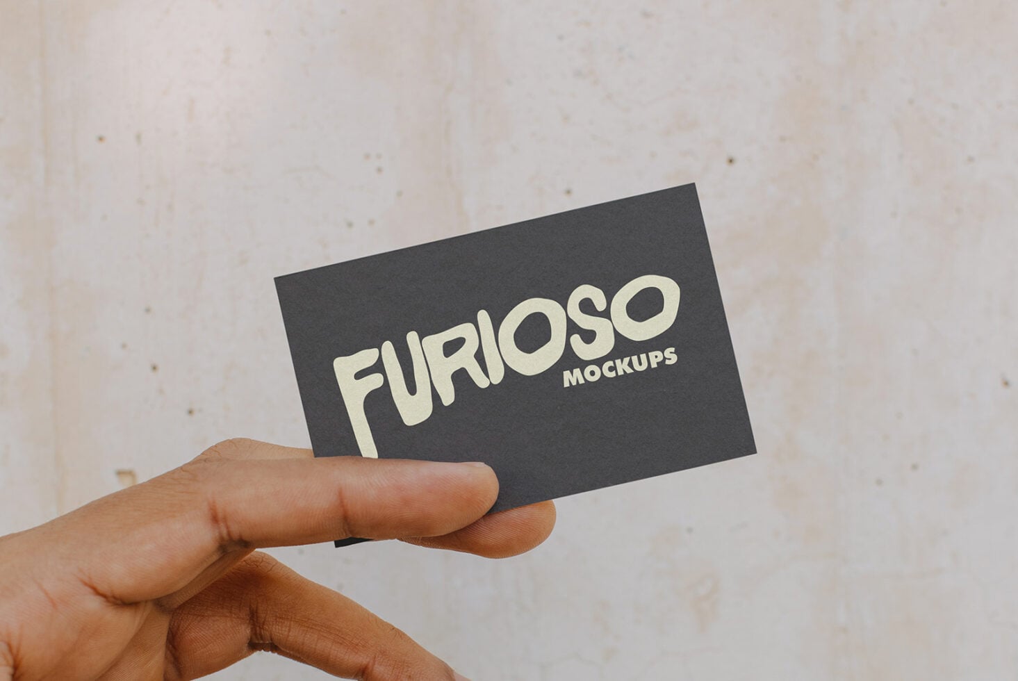Person holding dark card showing cream Furioso Mockups wordmark on neutral textured wall
