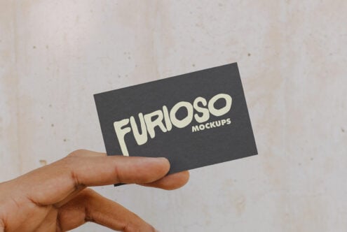 Person holding dark card showing cream Furioso Mockups wordmark on neutral textured wall