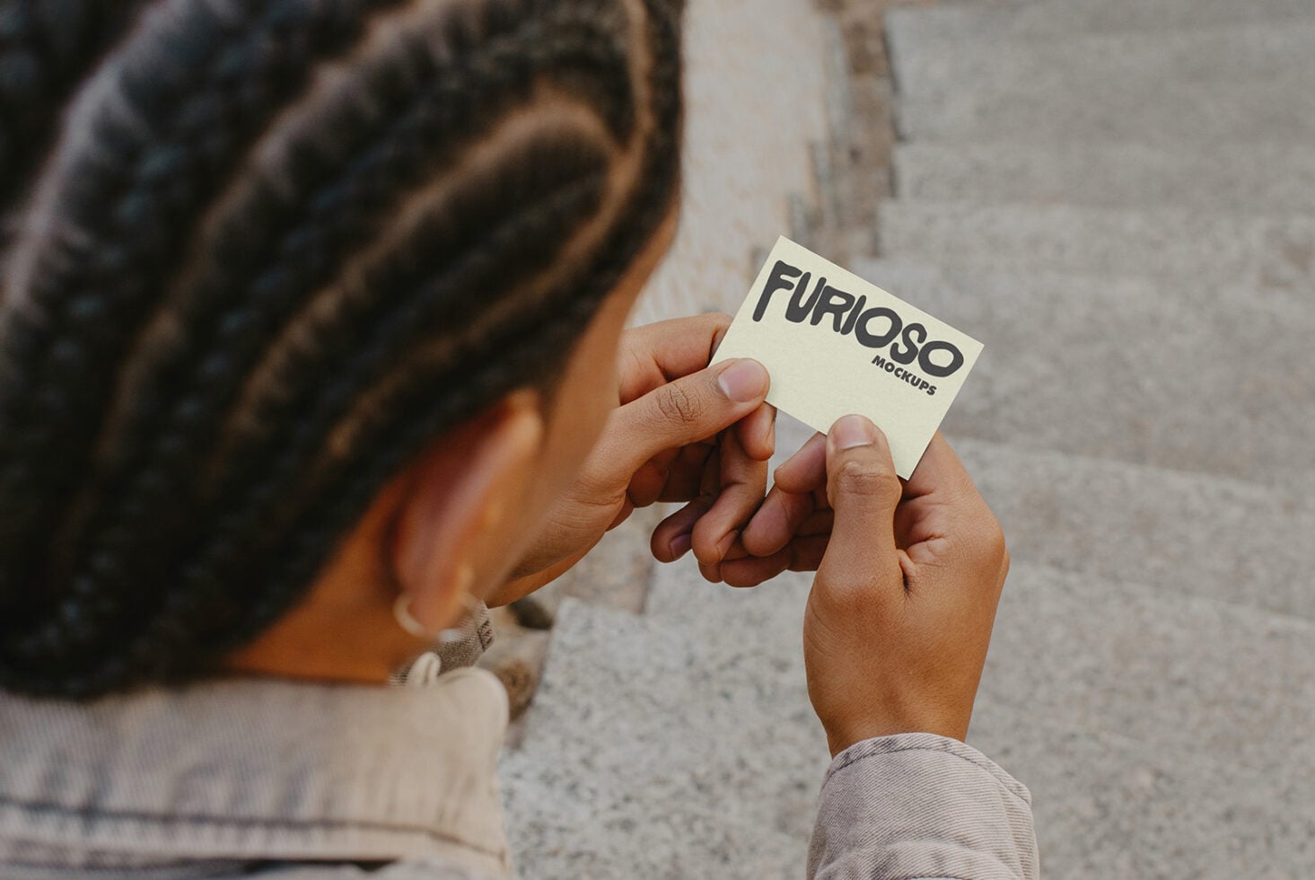Person showing off cream business card with Furioso Mockups text in outdoor urban setting