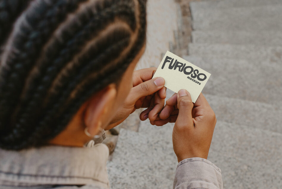 Person showing off cream business card with Furioso Mockups text in outdoor urban setting