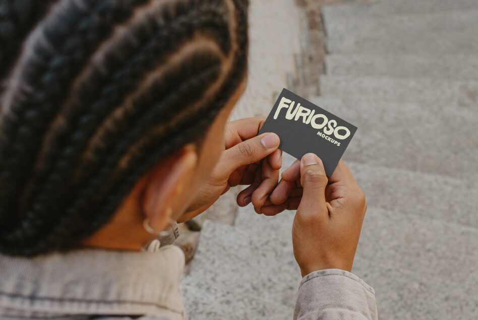 Close-up of hands holding dark business card displaying Furioso Mockups on concrete wall