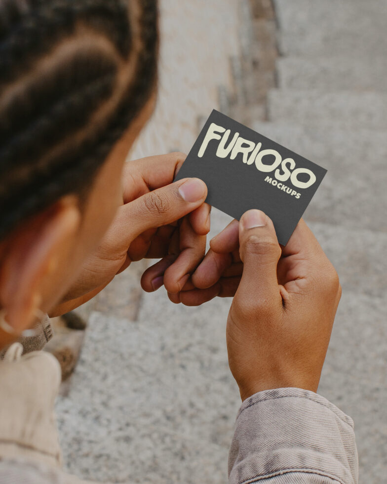 Two hands exchanging dark business card with Furioso Mockups text on concrete surface