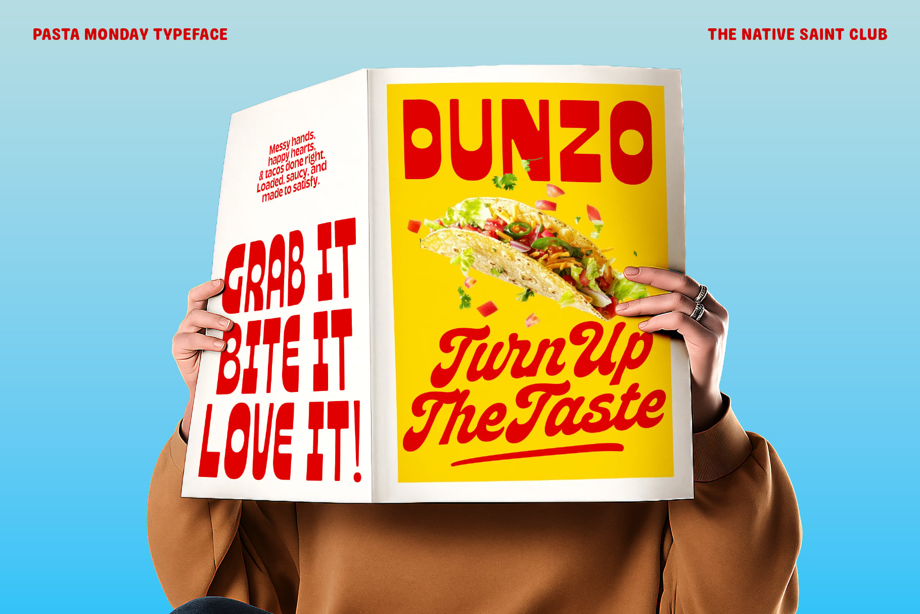 Open magazine spread with Dunzo taco design on yellow page held by hands against blue background