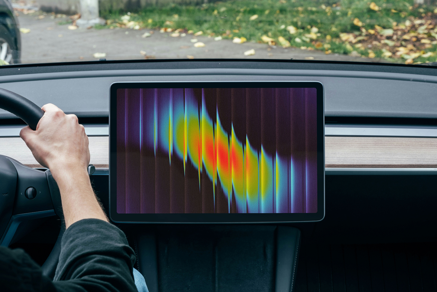 Car infotainment display showing colorful spectrum waveform with driver's hand on wheel