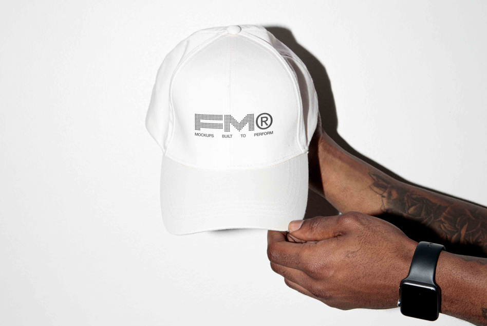 White baseball cap with FOM logo held in hands against neutral background
