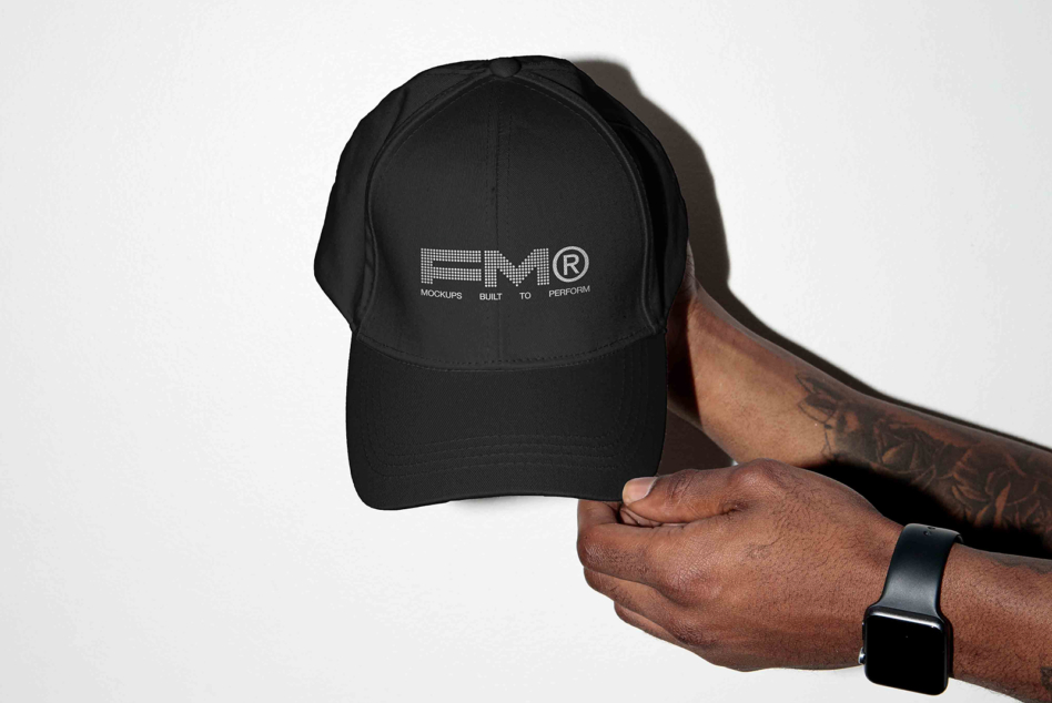 Black baseball cap with embroidered logo held in hands showing front detail