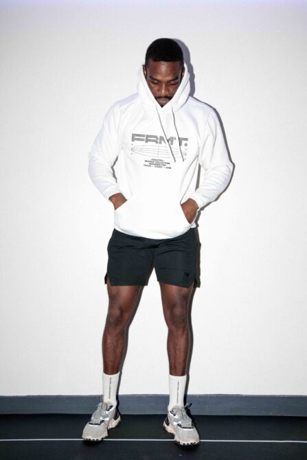 Guy in white hoodie with logo, black shorts, white socks, standing neutral pose
