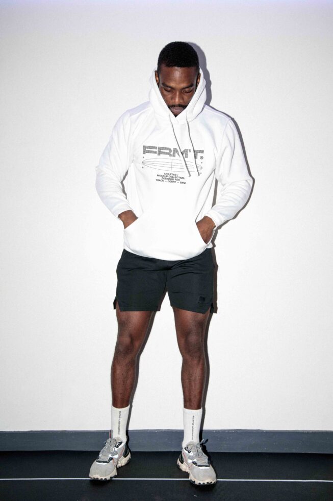 Guy in white hoodie with logo, black shorts, white socks, standing neutral pose