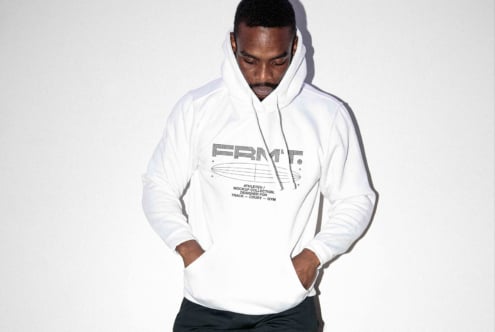 Guy in white hoodie with minimal logo design, looking down, hands at sides