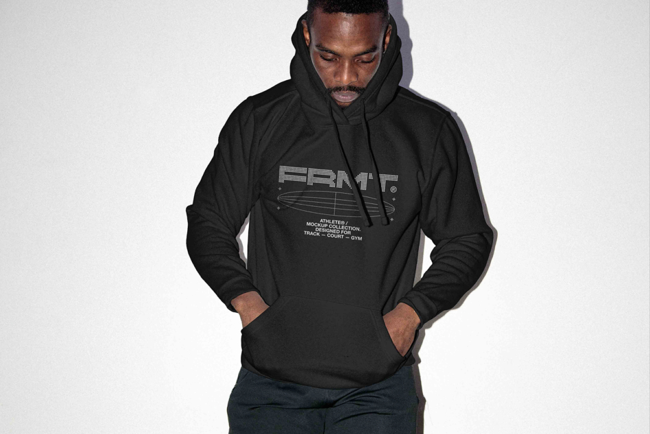 Man wearing black hoodie with geometric branding, hands in pockets, looking down