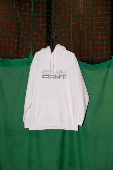 White hoodie hanging on net showing minimalist FRMT logo on green background