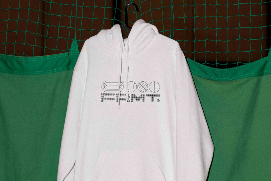 White hoodie on hanger with geometric logo print against green mesh backdrop