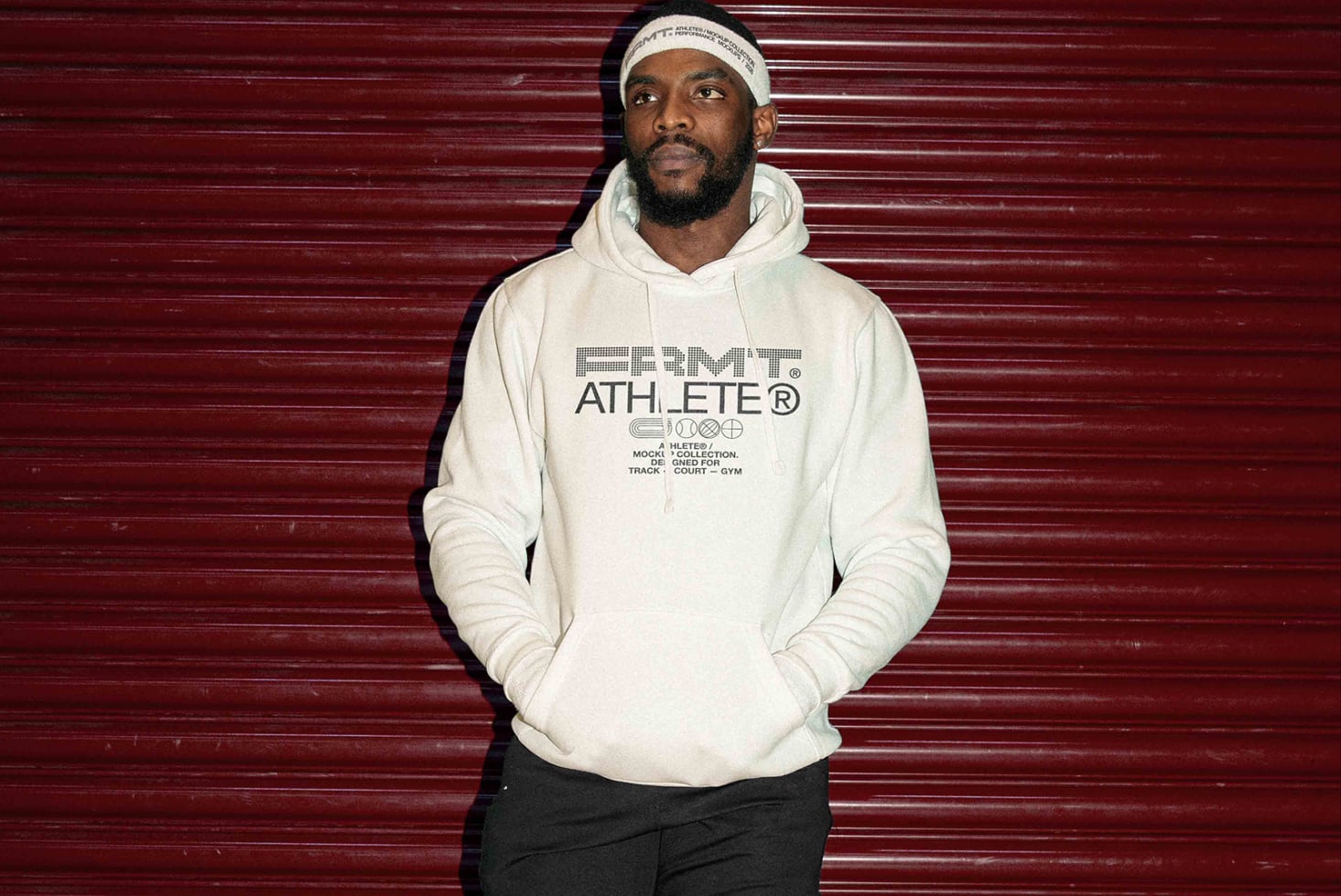 Dude in cream hoodie with outlined Athlete design on burgundy ribbed wall