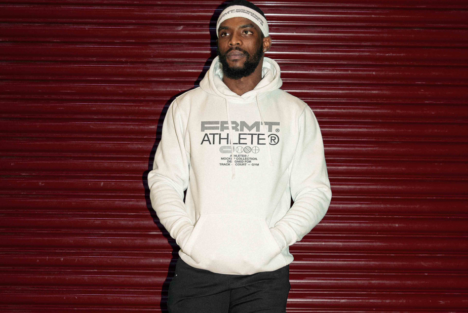 Dude in cream hoodie with outlined Athlete design on burgundy ribbed wall