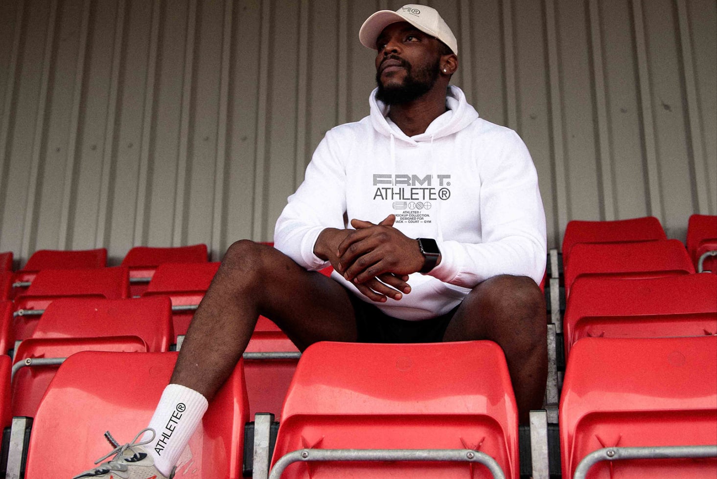 Man in white hoodie with FRMT Athlete logo sitting on red stadium seats
