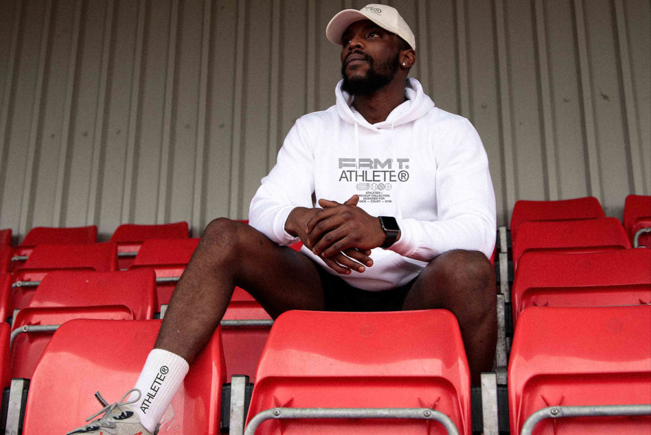 Man in white hoodie with FRMT Athlete logo sitting on red stadium seats