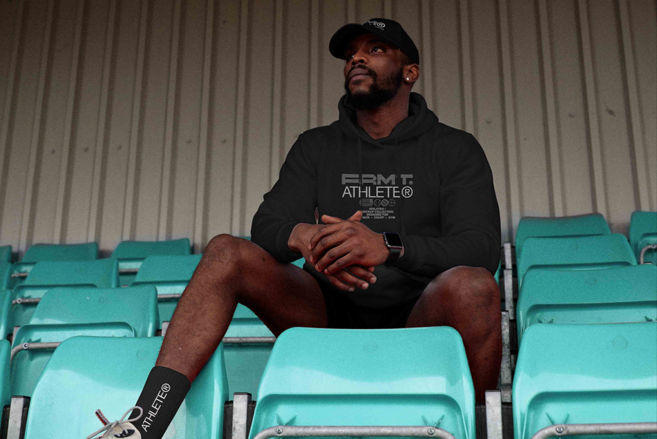 Man in black hoodie with cap sitting in stadium seats looking up