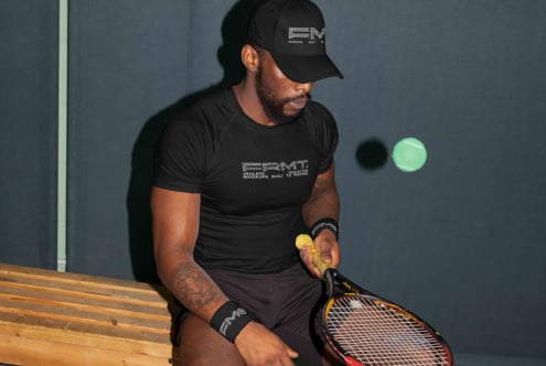 Tennis player in black branded tee on bench with racket looking away