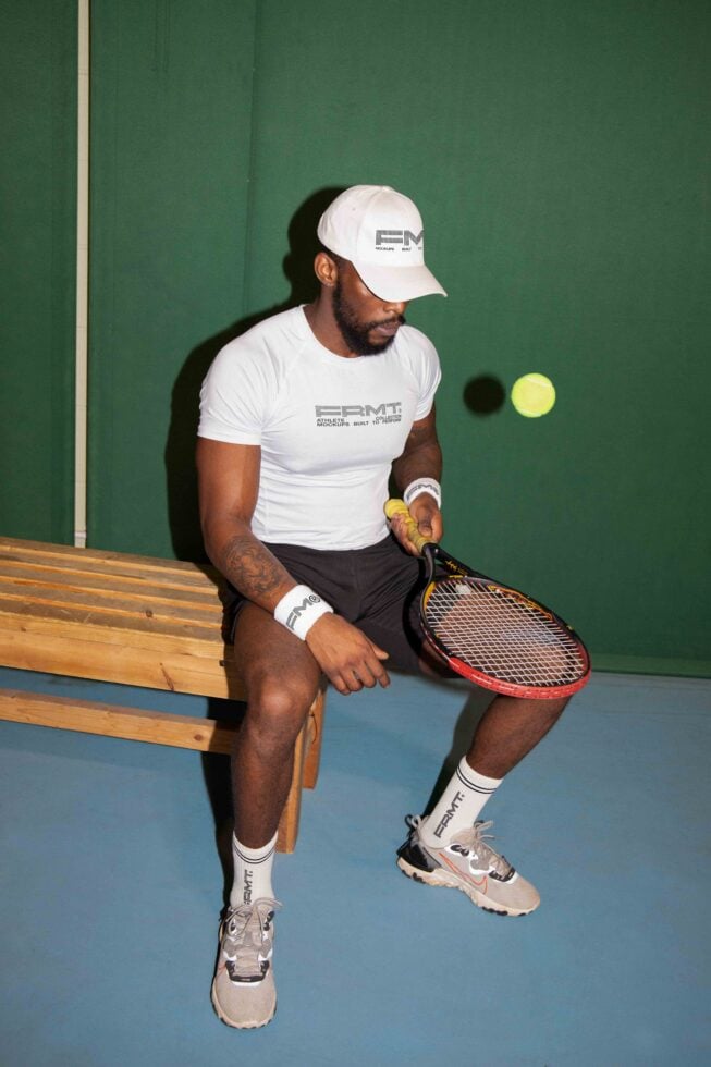 Tennis player in white branded tee sitting on bench holding racket