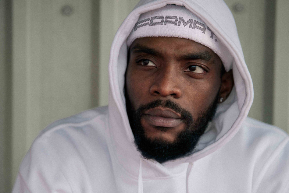Man in light pink hoodie with branded beanie gazing to the side