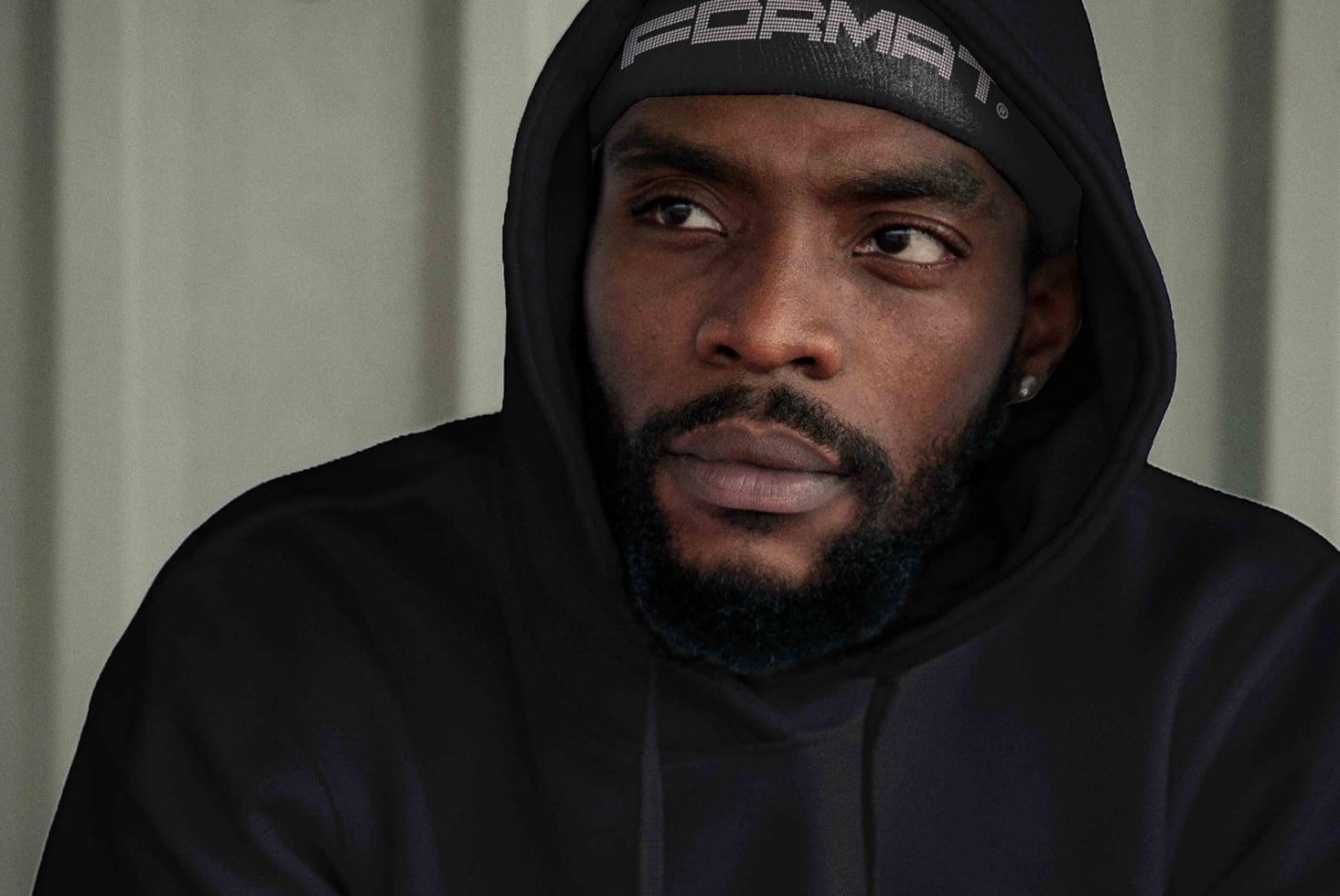 Man in black hoodie with branded beanie looking directly at camera
