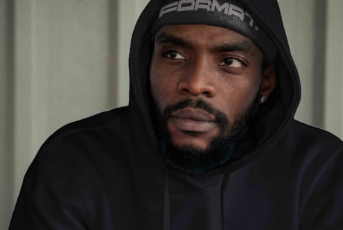 Man in black hoodie with branded beanie looking directly at camera