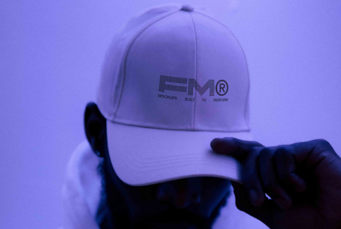 Light purple baseball cap with FRMT Athlete branding being held up in front of purple backdrop