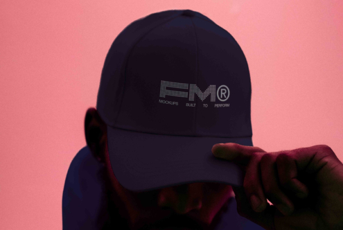 Black baseball cap with FRMT logo held up against warm coral pink background