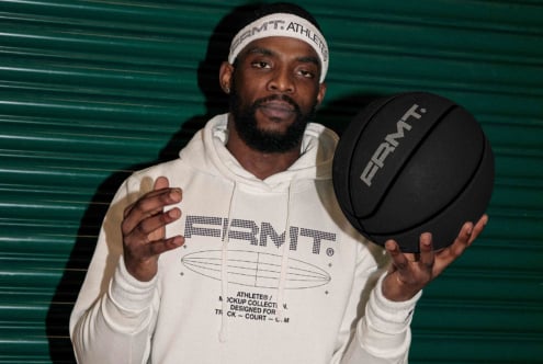 Dude in cream hoodie with teal backdrop holding black basketball