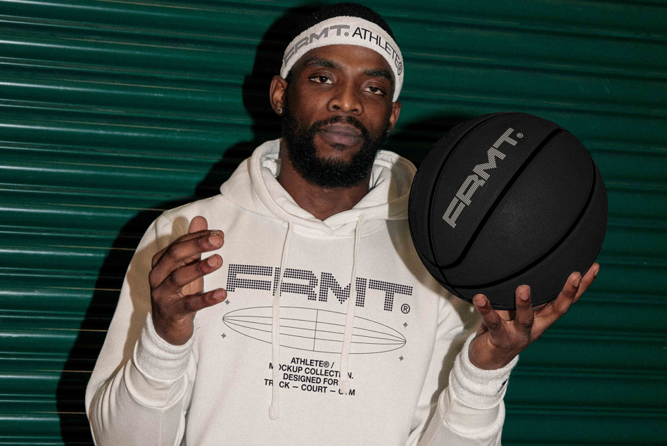Dude in cream hoodie with teal backdrop holding black basketball