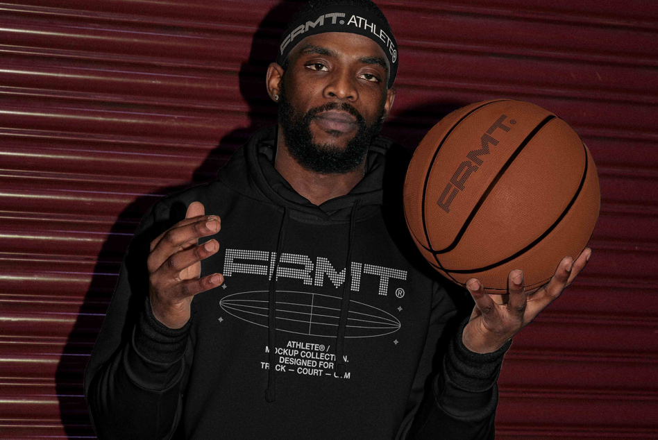 Man in black hoodie against burgundy backdrop holding tan basketball