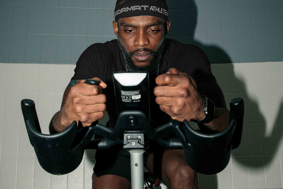 Guy on indoor bike holding handlebars with determined expression