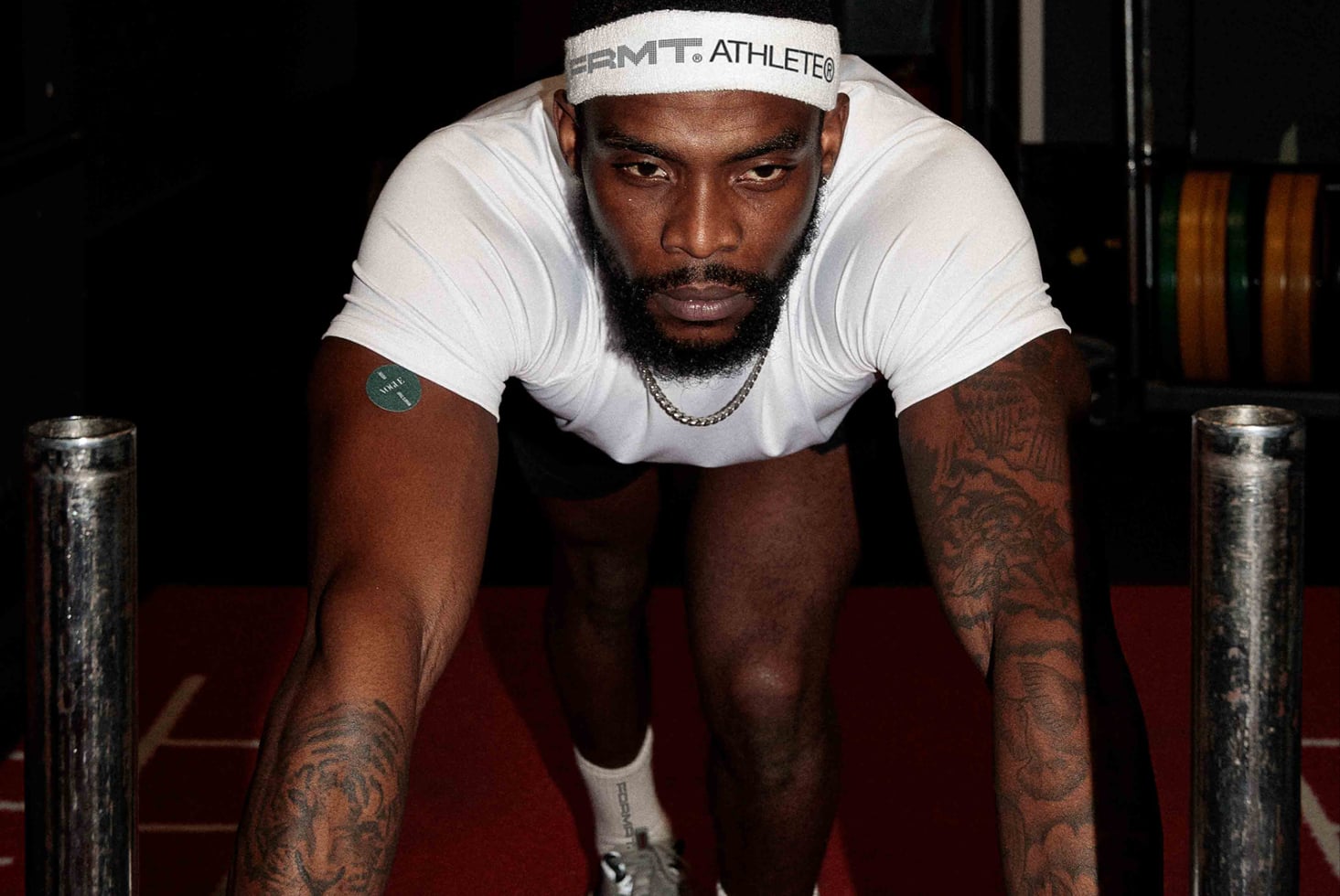 Athlete in white tank leaning forward on red mat focused