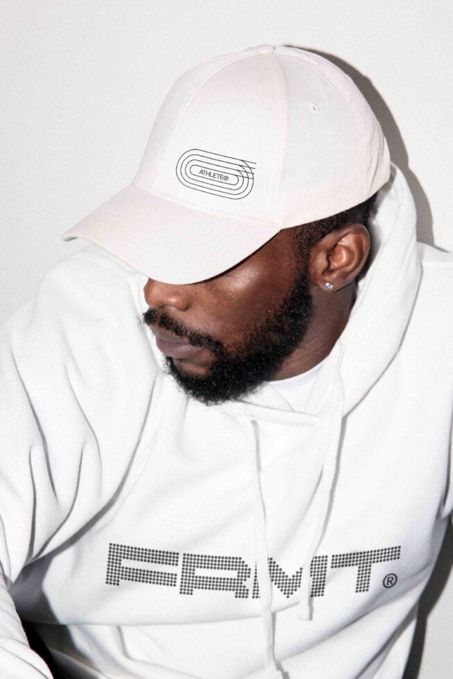 Man wearing white FRMT cap with line logo, white jacket detail from shoulders up
