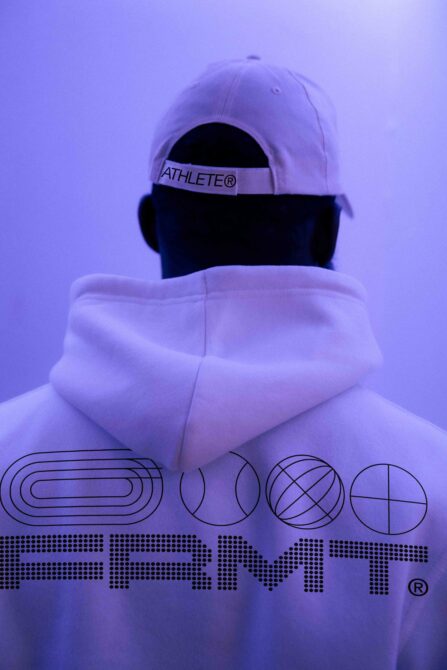 Figure from behind wearing white PRMT hoodie with geometric logo against purple glow