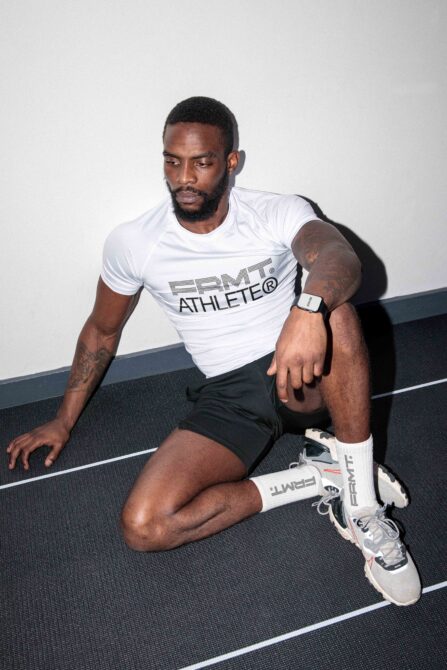 Guy sitting on court wearing white PRMT athlete tee with smartwatch visible on wrist