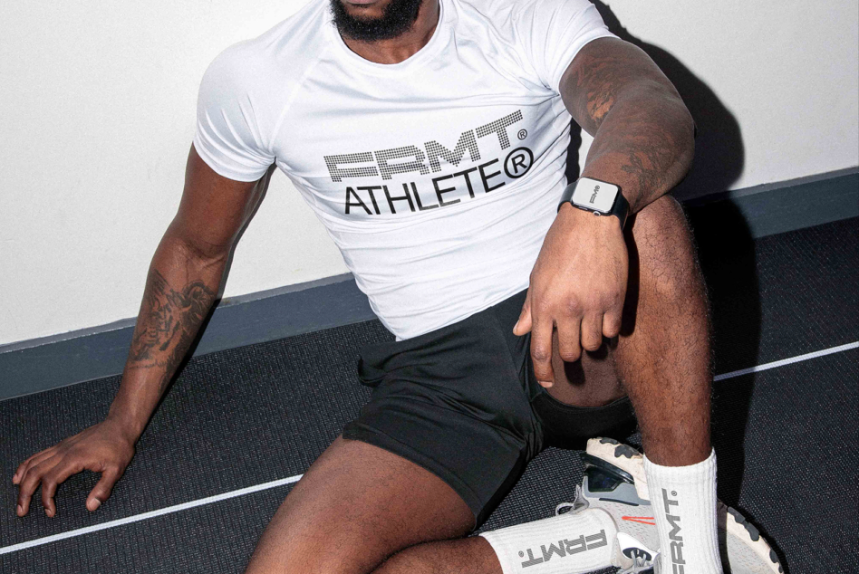 Athlete in white PRMT tee positioned low on court mat with smartwatch on wrist
