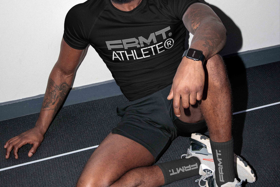 Man in black PRMT athlete shirt crouching on gym floor wearing smartwatch