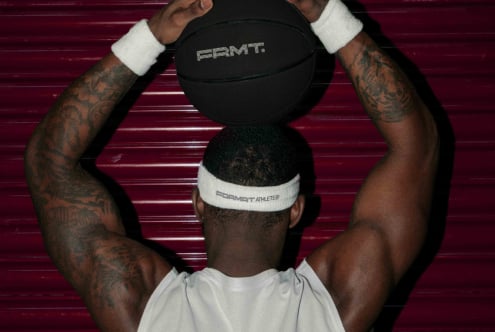 Athlete holding black basketball above head with white wristbands against burgundy metal backdrop