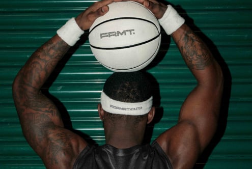 Shirtless athlete catching white PRMT basketball against green ridged wall background
