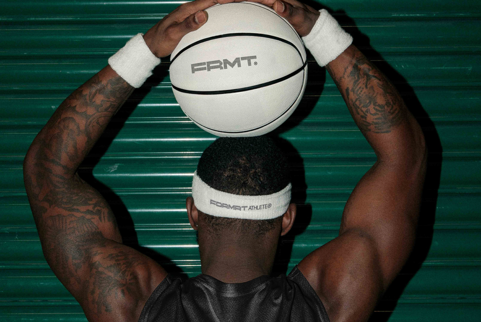 Shirtless athlete catching white PRMT basketball against green ridged wall background
