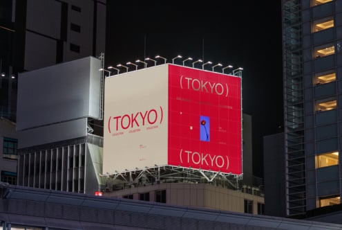 Night lit billboard showing Tokyo collection with red panel, buildings behind