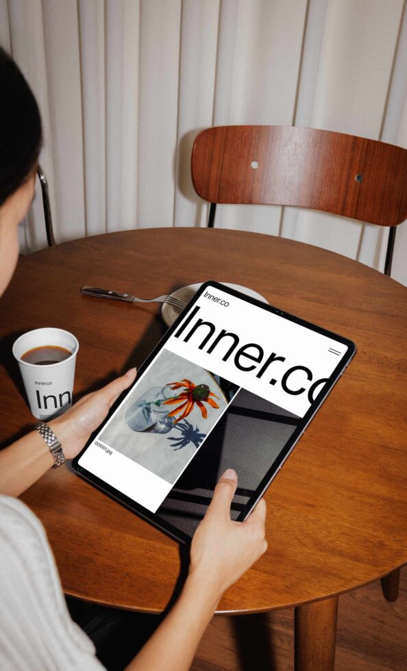 Tablet showing Inner.Co website with floral illustration, coffee cup branded with logo nearby
