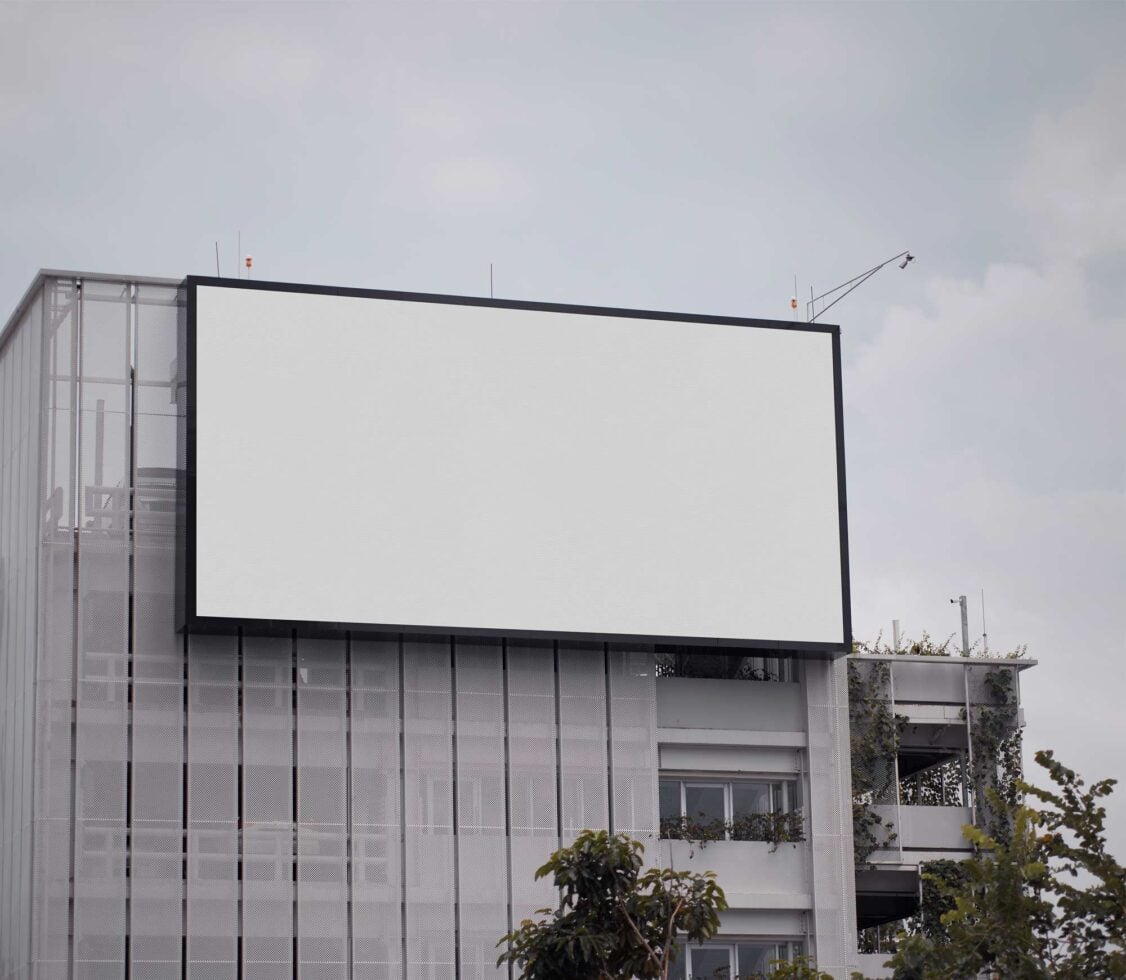 Blank billboard mounted on modern building facade with overcast sky
