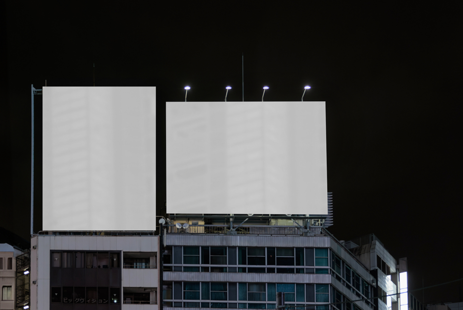 Two blank billboards on rooftop at night with floodlights illuminating them