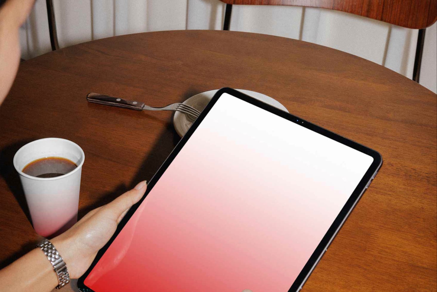 Tablet displaying white to red gradient screen on wooden table with coffee