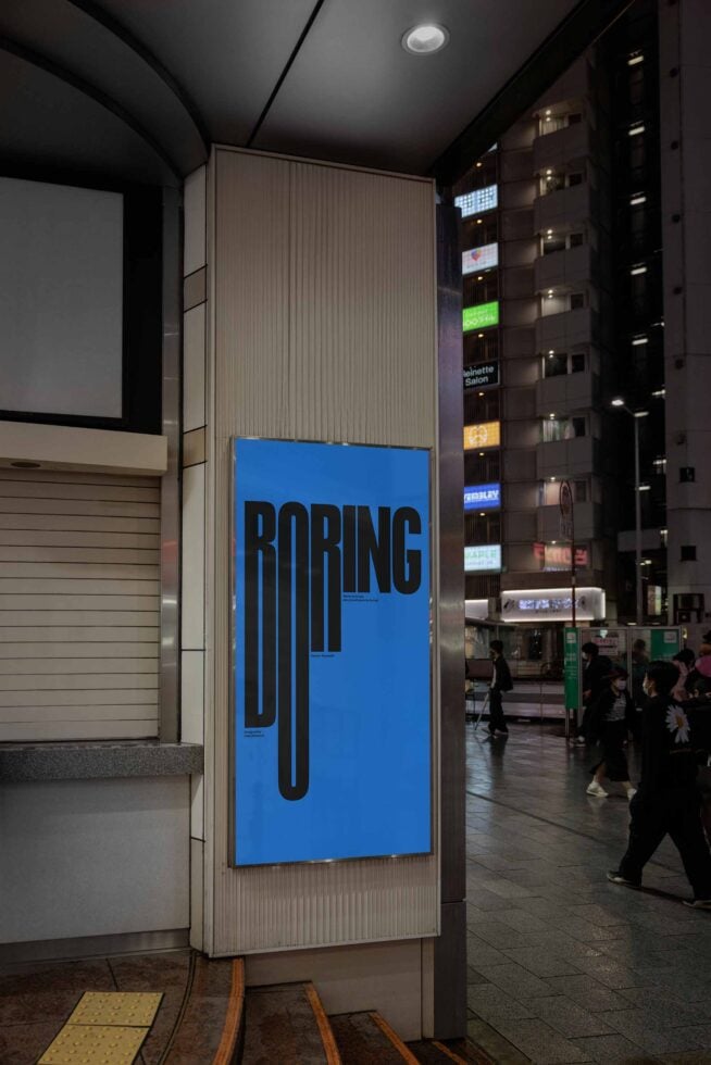 Vertical street-level billboard showing BORING text in black on blue background